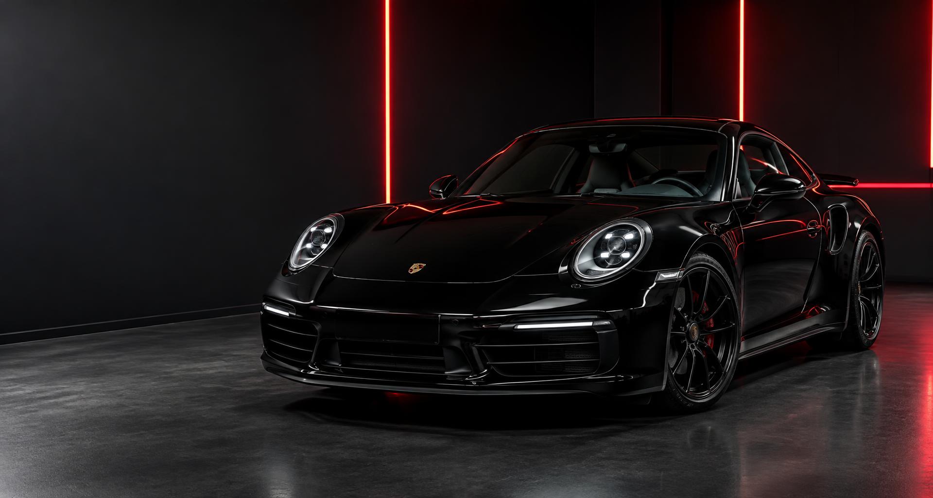 A meticulously polished black sports car in a red-lit detailing studio